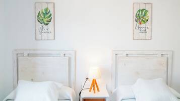 Deux lits avec du linge de lit blanc, une table de chevet avec une lampe et deux œuvres d’art murales représentant des feuilles tropicales.