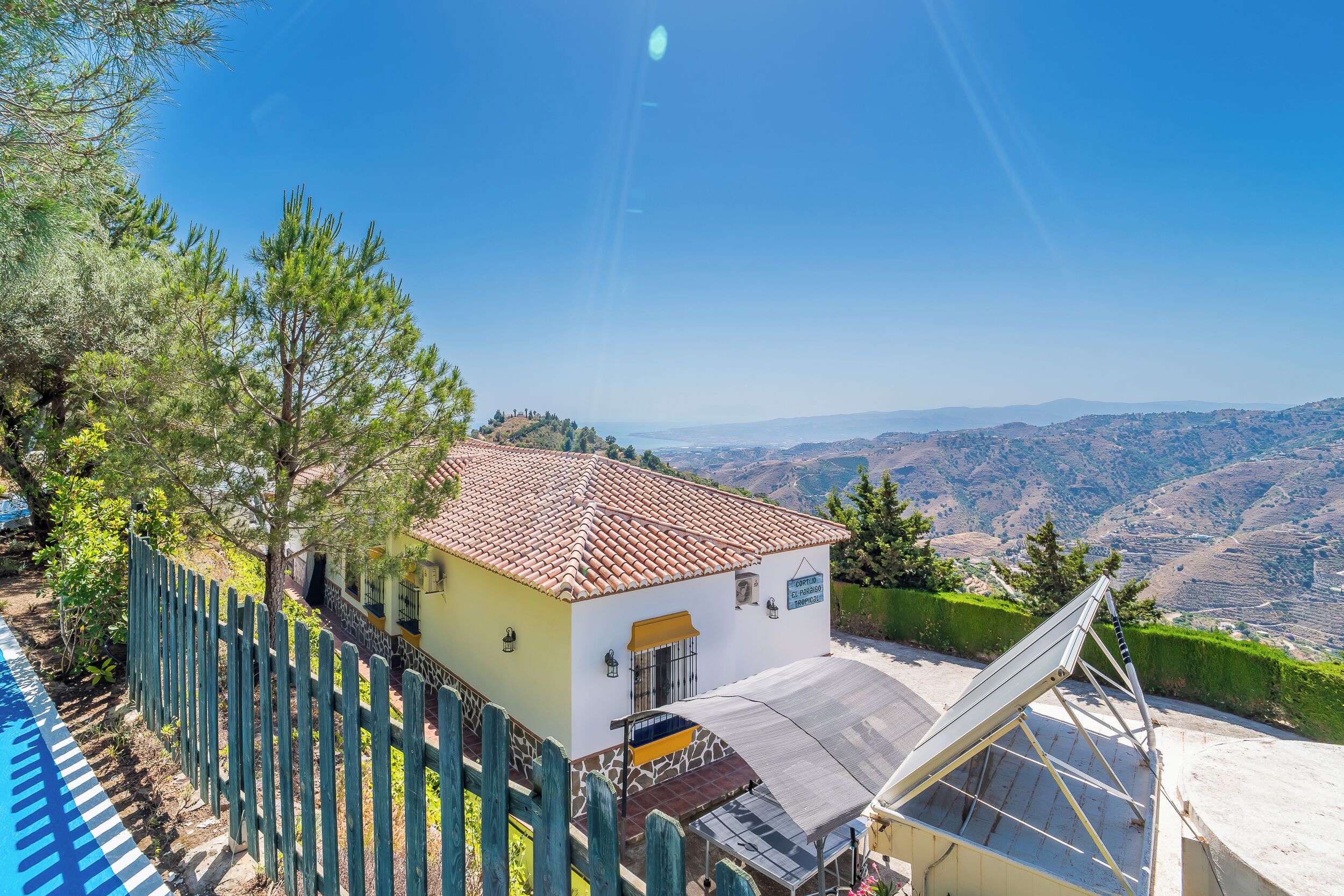 Une maison avec un toit en tuiles, un panneau solaire et une vue sur les collines.