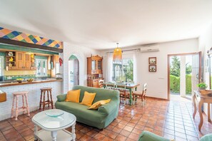 Un salón amplio con un sofá verde, una mesa de comedor y una cocina con armarios de madera y un salpicadero colorido.