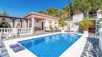 Une piscine avec des chaises longues, un patio couvert et un bâtiment blanc agrémenté de touches de jaune.