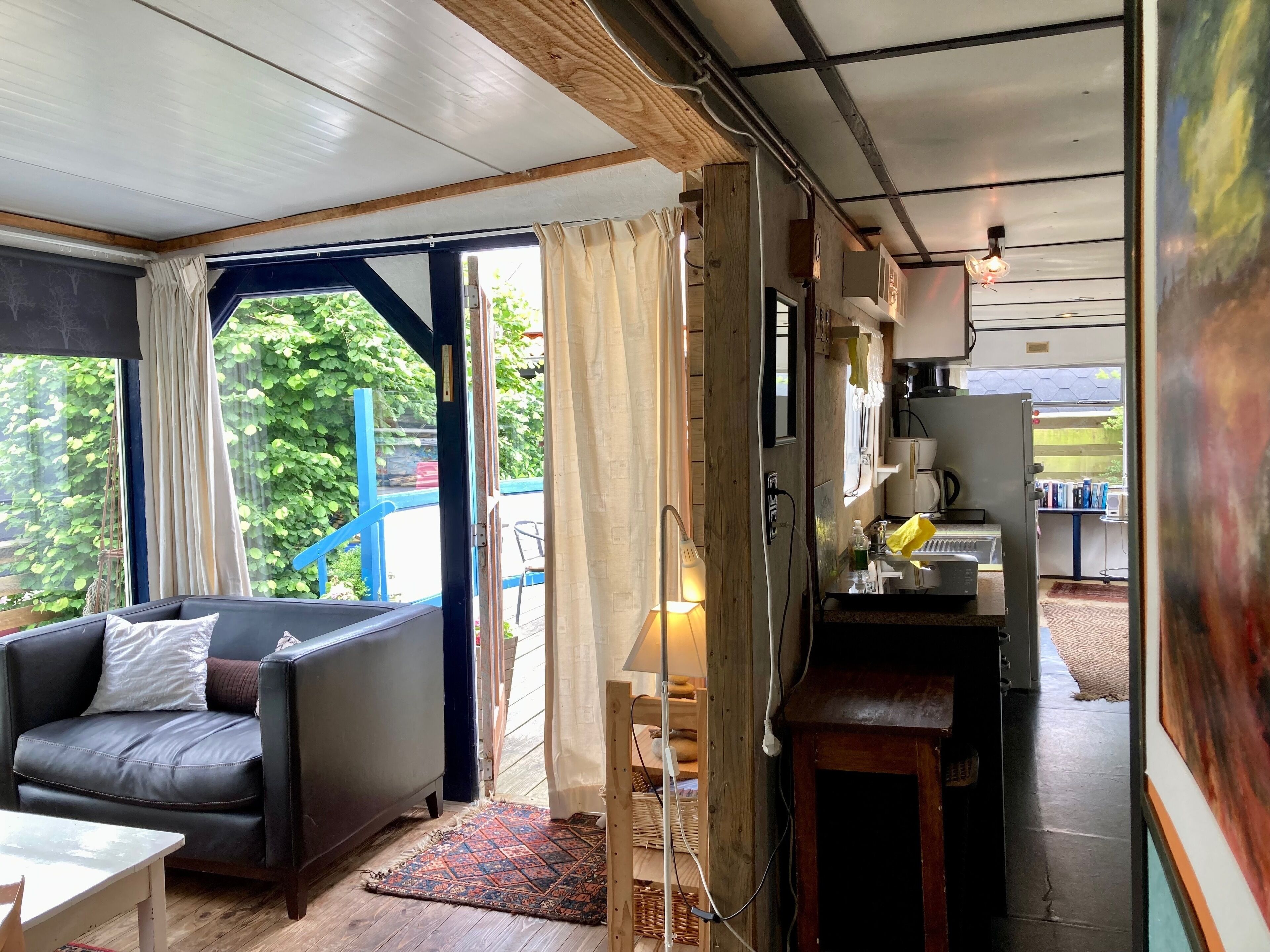 Een knus verblijf met een bank, een kleintje tafeltje, een kitchenette met waterkoker en uitzicht op groen.