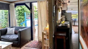 A cozy room with a sofa, a small table, a kitchen area with a kettle, and a view of greenery outside. - Beautiful quiet 2 persons caravan on the Lauwersmeer (Anjum)