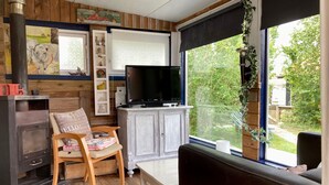 A cozy living room with a fireplace, a television, and a view of the outdoors. - Beautiful quiet 2 persons caravan on the Lauwersmeer (Anjum)