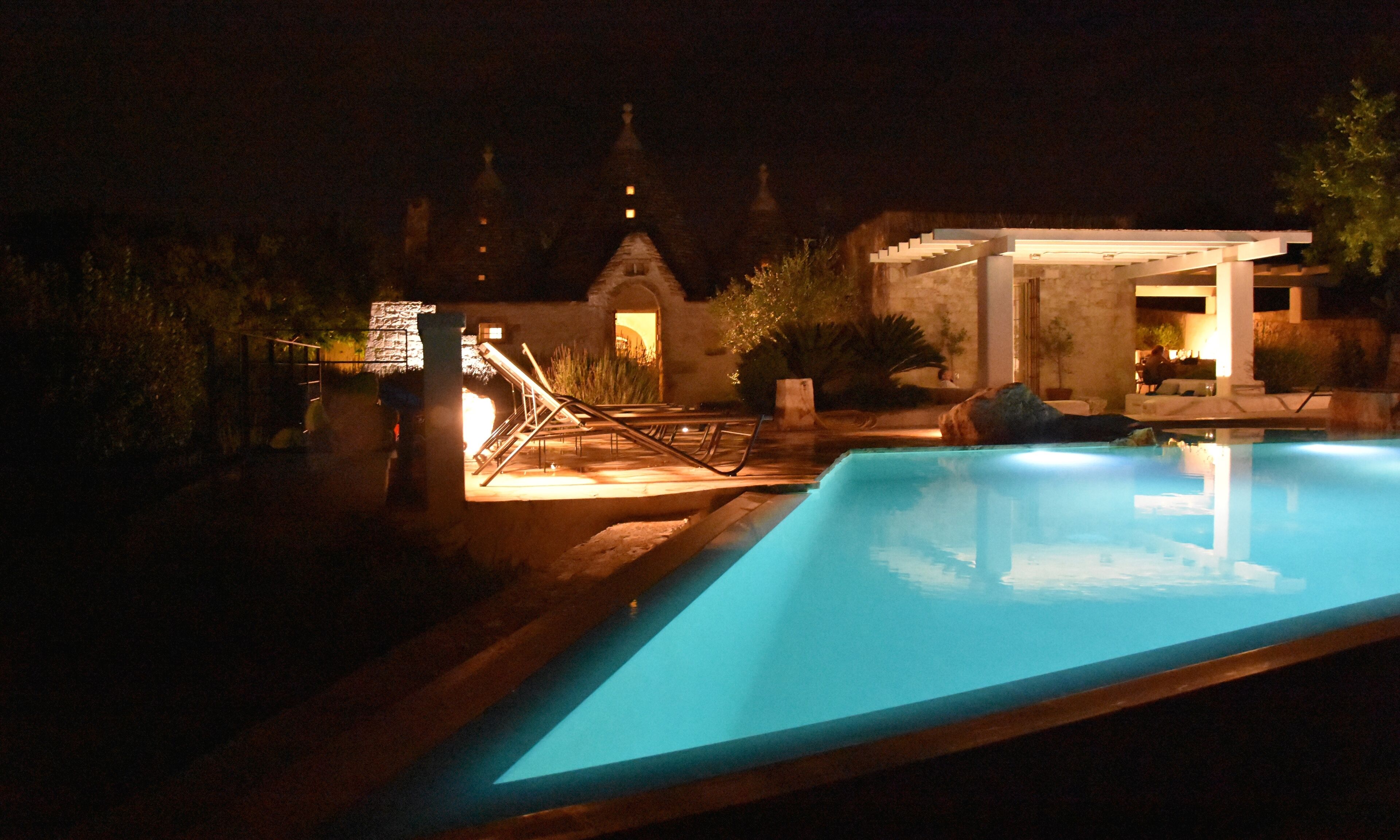Un espace piscine nocturne agrémenté d’un bâtiment en pierre et d’une pergola.