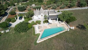 Eine Vogelperspektive auf ein Anwesen mit Schwimmbad, einem Haus mit Kegeldächern und umgebender Vegetation.