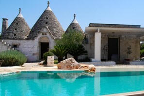 Un edificio de piedra con techos cónicos, una piscina y una gran roca al frente.