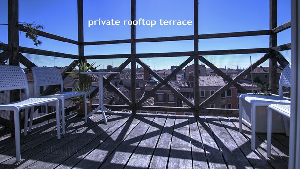 Una terrazza privata sul tetto con pavimento in legno, sedie bianche e vista sulla città.