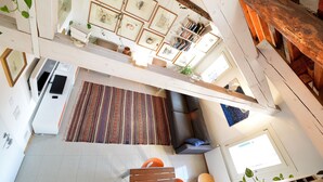 Un'ampia zona giorno con un divano grande, un tavolino da caffè e un tappeto decorato. Si vede una scala che collega due livelli, e una libreria piena di libri e oggetti decorativi.