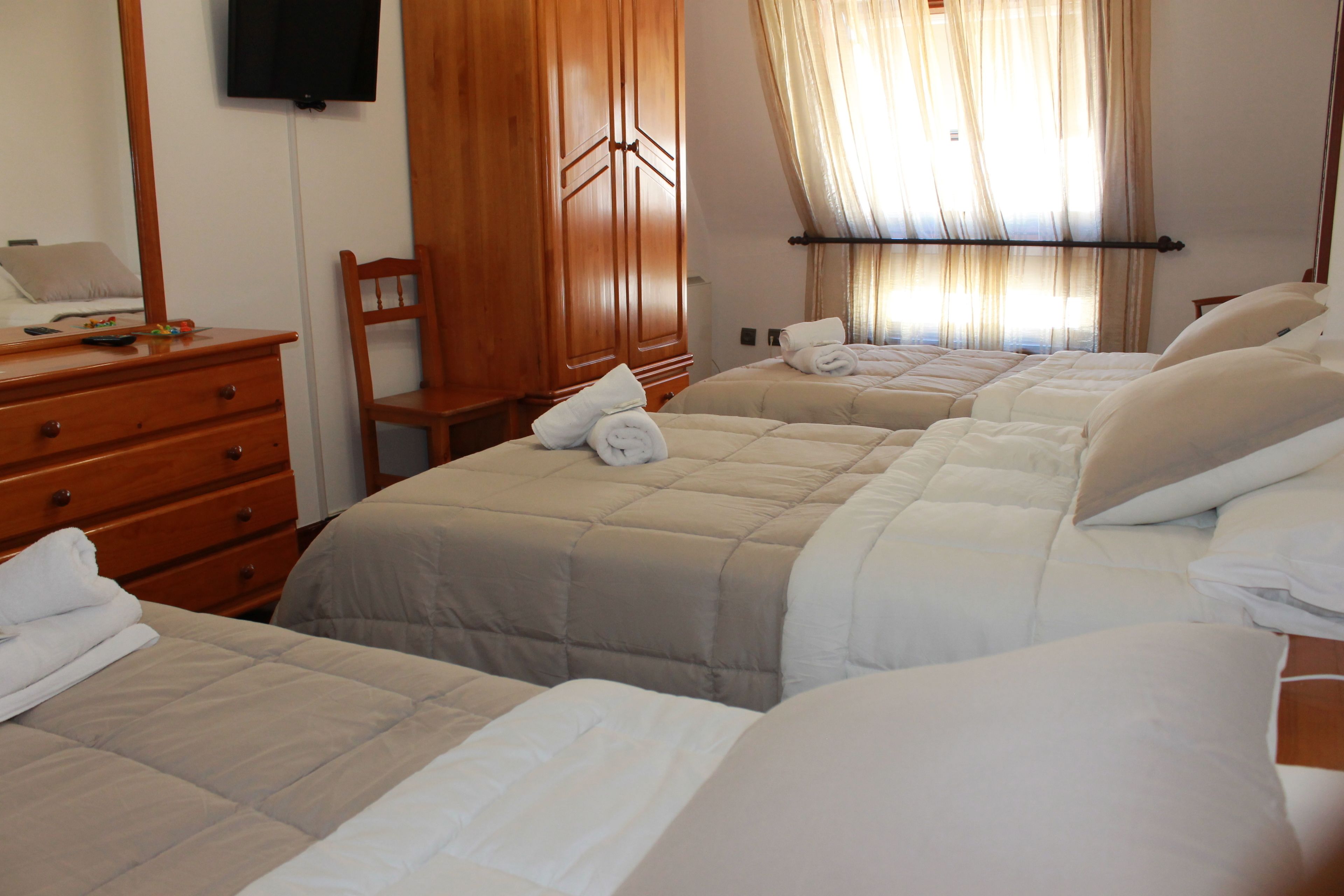 A hotel room with two beds, a wooden dresser, a chair, and a television mounted on the wall.