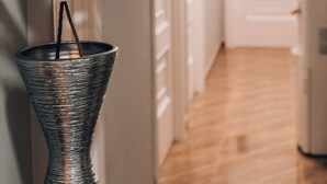 A hallway with a plant in a textured vase, a door at the end, and a wall with a decorative piece. - Pension As Burgas (Caldas de Reis)