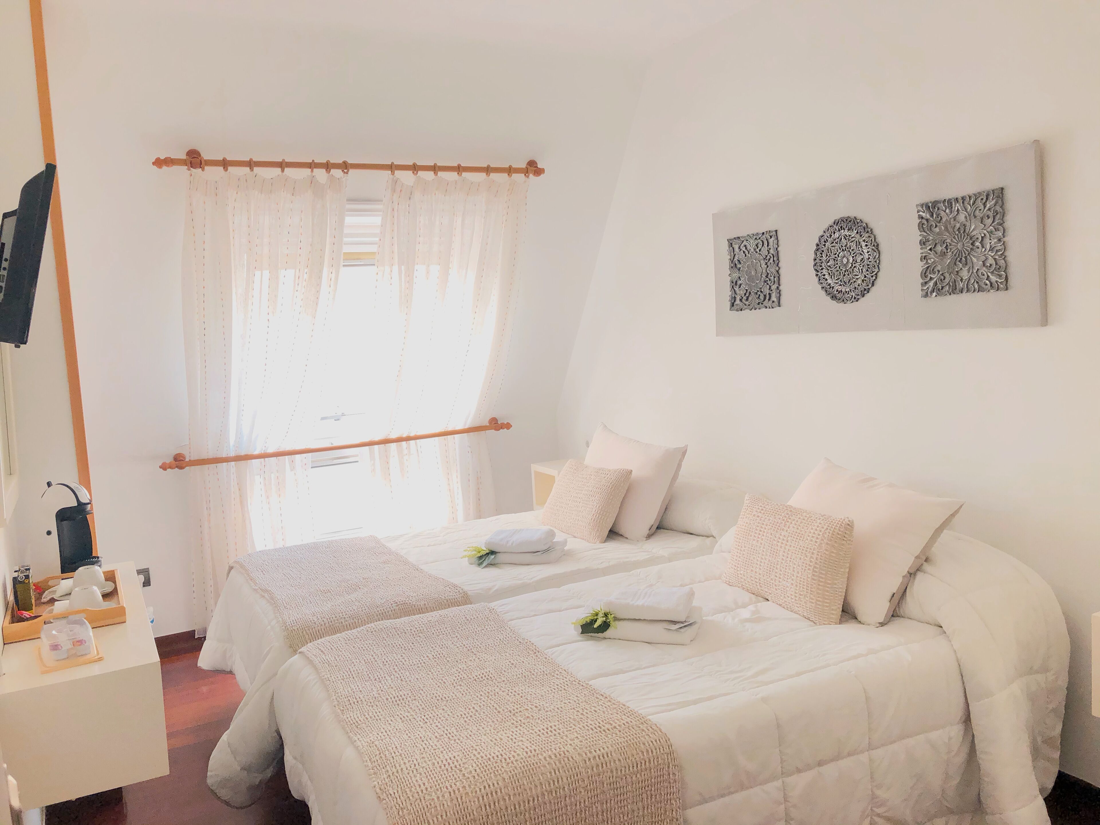 Habitación de hotel con dos camas, cabecero de madera, una mesita con artículos de aseo y decoración en la pared.
