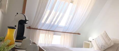 A bedroom with a bed, a bedside table, a lamp, and a window with sheer curtains.