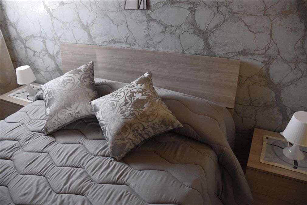 Un lit bien fait, avec une couverture grise et deux coussins à motifs, une tête de lit en bois et des lampes de chevet posées sur des tables de nuit en bois.