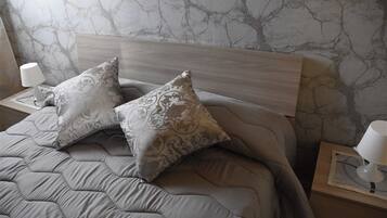Un lit bien fait, avec une couverture grise et deux coussins à motifs, une tête de lit en bois et des lampes de chevet posées sur des tables de nuit en bois.