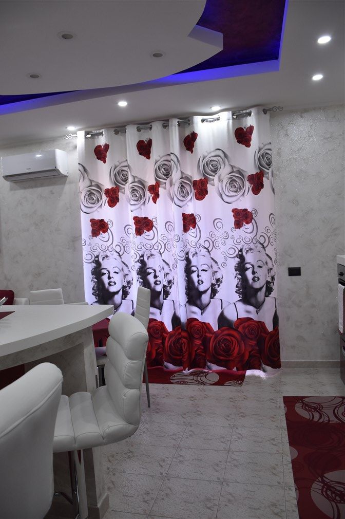 A dining area with a white table, white chairs, and a curtain with a rose pattern.