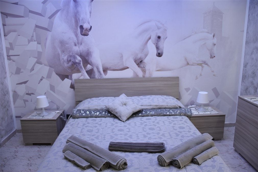 Ein Schlafzimmer mit einem großen Bett, zwei Nachttischen und einer Wandmalerei von Pferden.