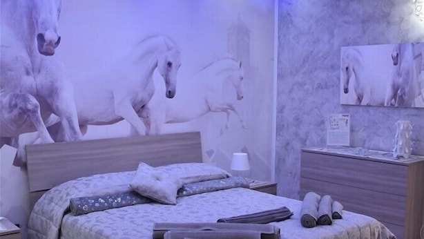 Un dormitorio con cama, mesita de noche, aire acondicionado montado en la pared y una pared decorada con motivos de caballos.