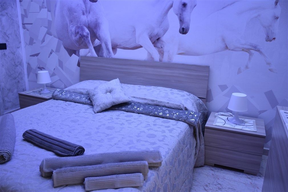 A bedroom with a bed, pillows, a nightstand, and a wall mural of horses.