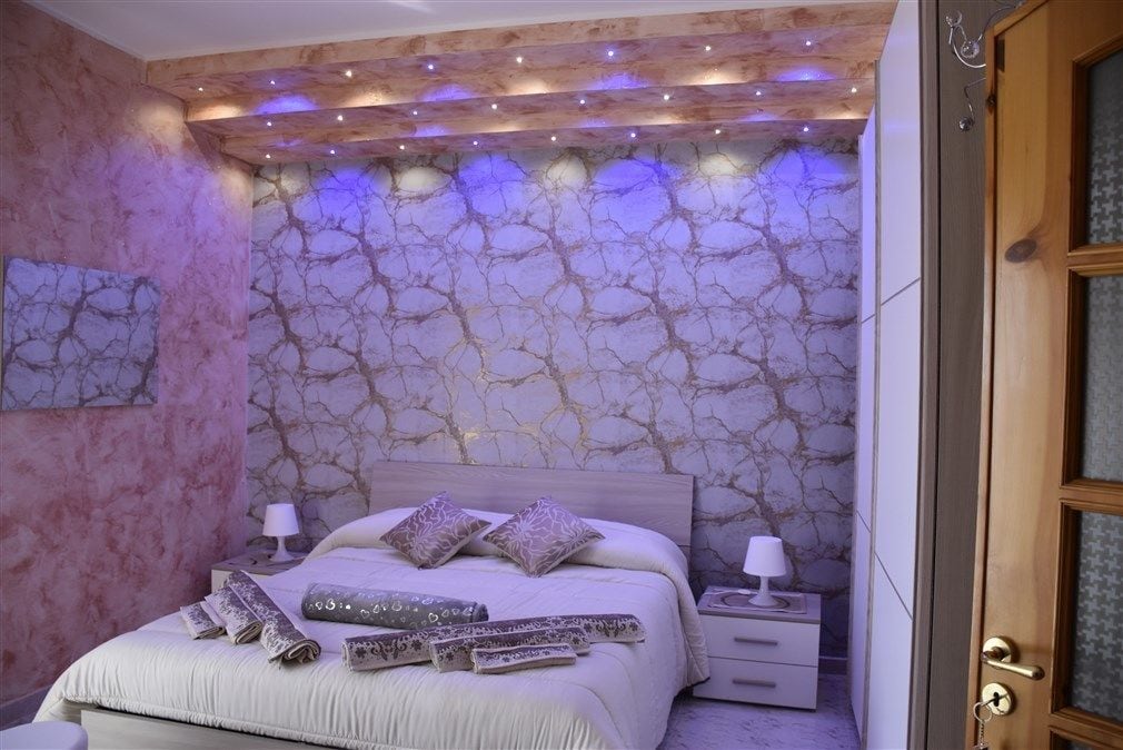 Un dormitorio con pared de diseño de mármol, una cama con abundantes almohadas y lámparas de noche.