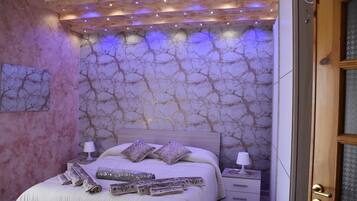 Un dormitorio con pared de diseño de mármol, una cama con abundantes almohadas y lámparas de noche.