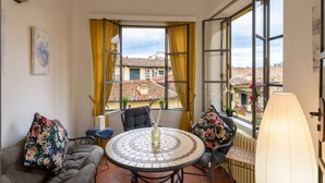 A cozy room with a round table, two chairs, a sofa, and a view of buildings through large windows with yellow curtains. - EXCLUSIVE SUITE with Amazing Terrace in the heart of Florence Ponte Vecchio (Firenze)