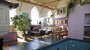 A spacious living room with a pool table, a large potted plant, and a dining area.