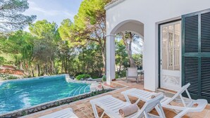 Una piscina con sillas de descanso blancas y una pérgola.