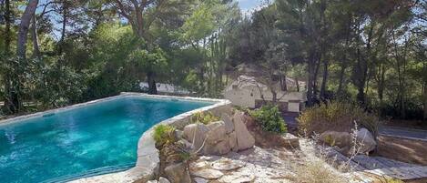 A swimming pool surrounded by natural landscape and stone architecture.