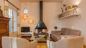 Una sala de estar con chimenea, dos sillones, un sofá, un televisor y estantes decorativos.
