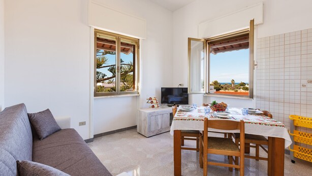 A compact living space with a sofa, a dining table with chairs, a TV, and a small kitchen area.