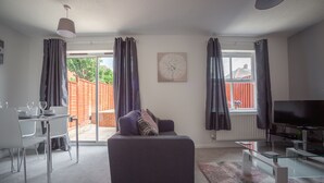 A modern living room with a sofa, TV, and dining area. - HEREFORD – Kestrel House: 4-Bed Home North of City, Parking for 2, Sleeps 7 (Hereford)