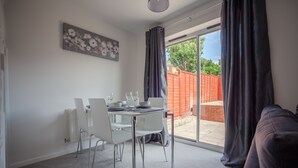 A dining area with a table set for four, a white chair, and a gray couch. - HEREFORD – Kestrel House: 4-Bed Home North of City, Parking for 2, Sleeps 7 (Hereford)