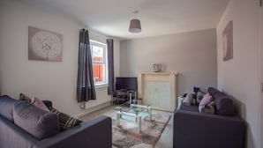 A living room with two sofas, a glass coffee table, a fireplace, and a television. - HEREFORD – Kestrel House: 4-Bed Home North of City, Parking for 2, Sleeps 7 (Hereford)