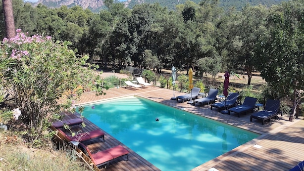 A wooden deck with a swimming pool, lounge chairs, and a view of mountains. - COMFORTABLE CHALET HEATED POOL BEACHES AND RIVER 10 MIN AWAY (Conca)