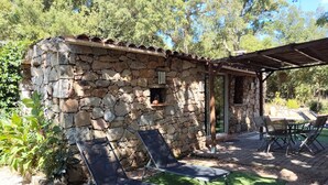A stone building with a tiled roof, a covered patio area with a table and chairs, and two lounge chairs on a grassy area. - COMFORTABLE CHALET HEATED POOL BEACHES AND RIVER 10 MIN AWAY (Conca)