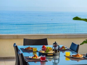 Un tavolo imbandito con prodotti per la colazione, una caffettiera e vista sul mare.
