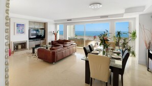 A modern living room with a large sofa, a dining table set for four, and a kitchen area. - 405 Luxury 4 Bed Penthouse, Heated 20m Pool-Front Line-Paseo-Bikes-BBQ-Hot Tub (Estepona)