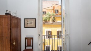 A room with a wooden cabinet, a framed picture, and a view of a yellow building through an open door.