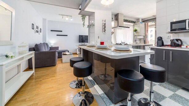 Eine moderne Küche mit Kochinsel, Barhocker, einer Essecke mit einer Couch und einem Fernseher.