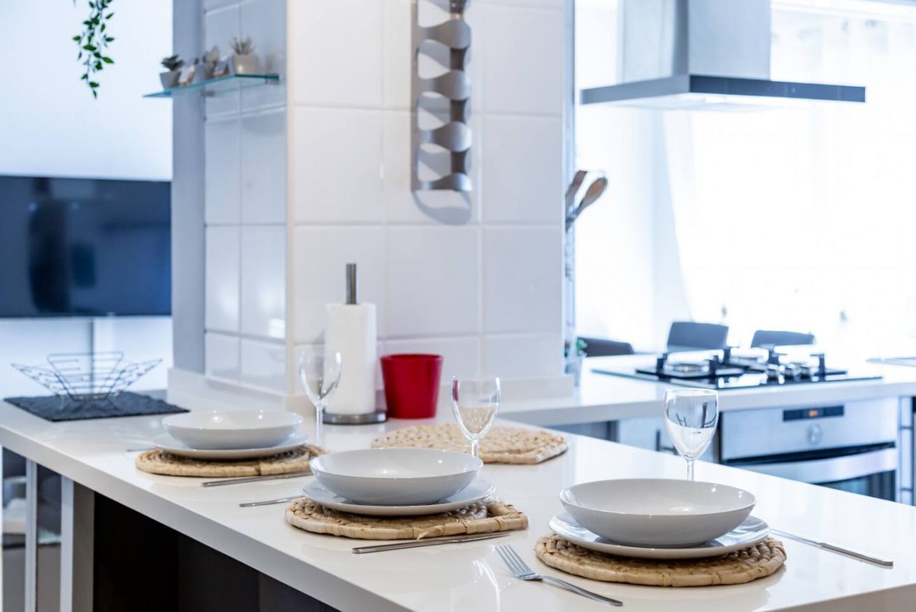 A modern kitchen with white countertops, a central island with a glass top, and a stainless steel range hood.