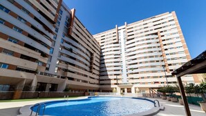Ein modernes Apartmenthaus mit einem zentral gelegenen Schwimmbad, umgeben von einer gepflasterten Fläche.