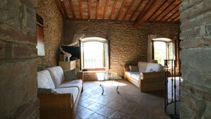 Una habitación rústica con paredes de piedra y un alto techo de madera, amueblada con sofás blancos y una mesa de centro de vidrio.