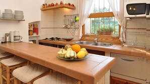 Uma cozinha com ilha central, banquetas, micro-ondas e uma janela com cortinas.