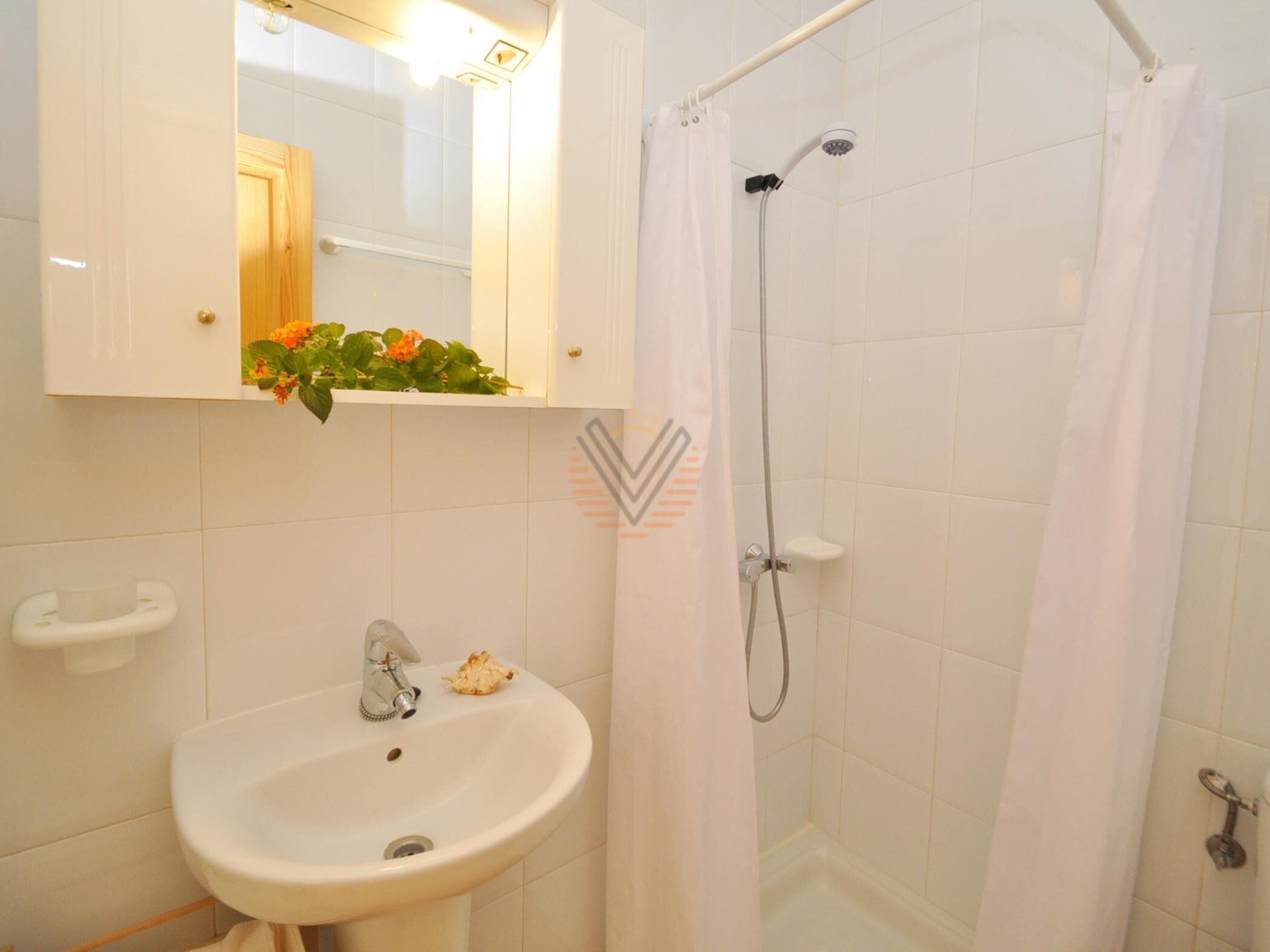 Een badkamer met een wit wastafelmeubel, een spiegel, een douche en een toilet.