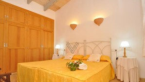 Quarto com cama, guarda-roupa de madeira, duas luminárias na parede e uma pequena mesa com abajur.