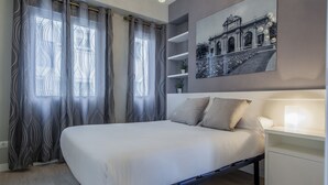 Une chambre moderne avec un lit, des rideaux, une table de chevet, une lampe et une étagère murale agrémentée d’une plante.