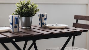 Une table en bois, un pot en métal, deux tasses à motifs et une assiette blanche.