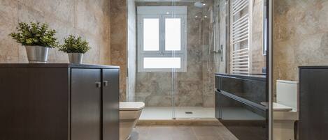 Un baño moderno con ducha envuelta en cristal, inodoro y tocador con gabinete.