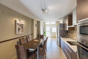 A modern kitchen with a built-in oven, a dining area with a long table and chairs, and a view into the adjacent living area.