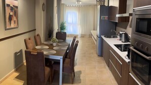 A modern kitchen with a dining area, featuring a built-in oven, a refrigerator, and a sink.